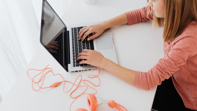 A teenage girl with headphones concentrating on a laptop