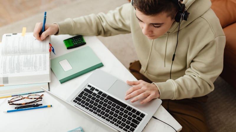 A teenager working at a laptop with headphones on