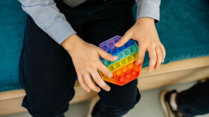 A child’s hands pressing the bubbles of a rainbow fidget toy
