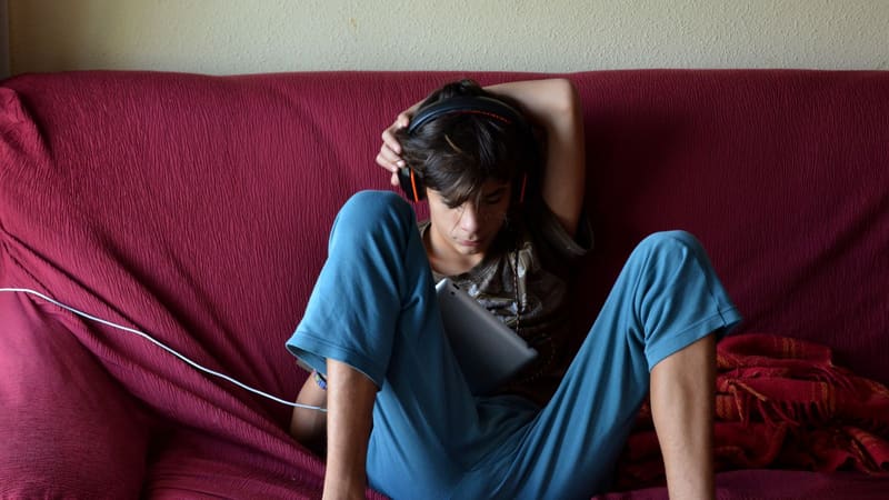A boy wearing headphones using a tablet on a sofa