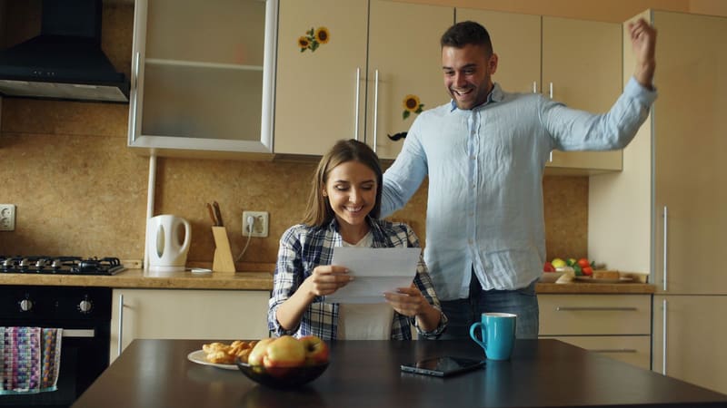 A couple in a kitchen reading a letter together and smiling