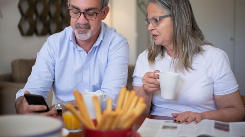 An older couple reading something on a phone together over coffee