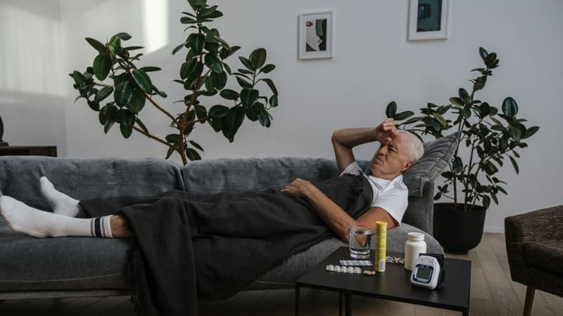 A man resting on a sofa with medicines on the table
