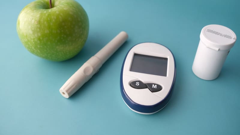 A glucose monitor, an insulin pen and an apple on a table
