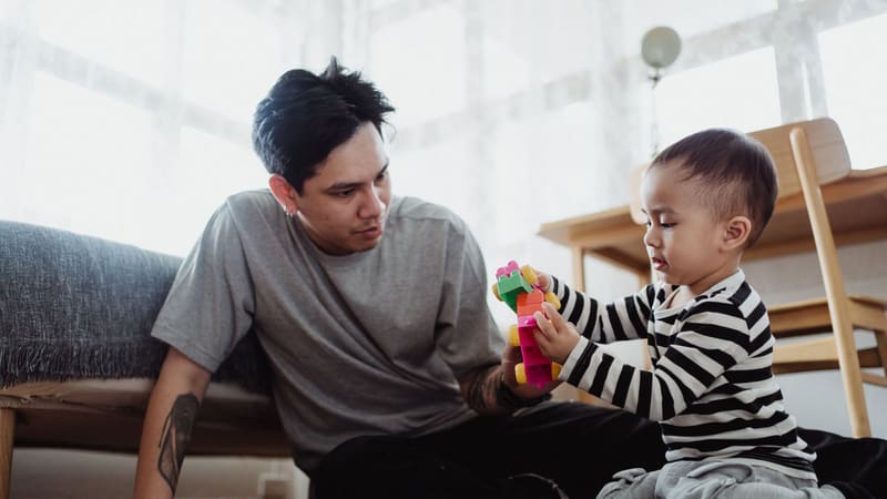A father and his young son building with coloured blocks on the floor