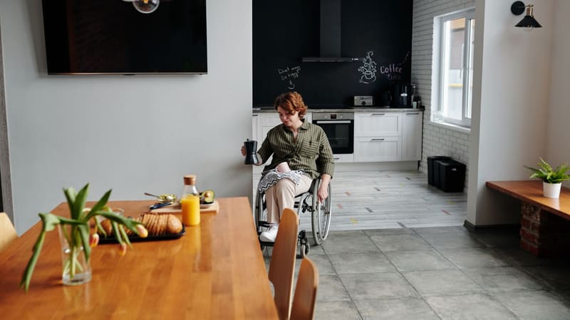A woman in a wheelchair holding a coffee in her kitchen
