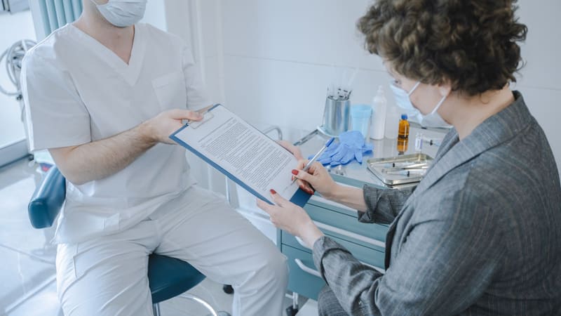 A patient signing a form across a desk from a health professional