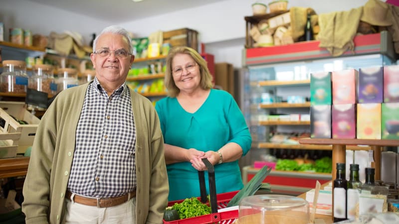 An older couple smiling while choosing groceries in a small shop