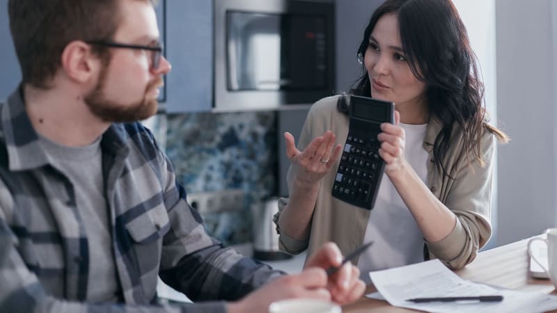 A woman working out a budget with a calculator at a kitchen table
