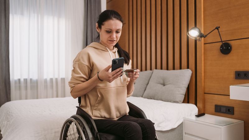 A woman in a wheelchair checking her phone while holding a bank card