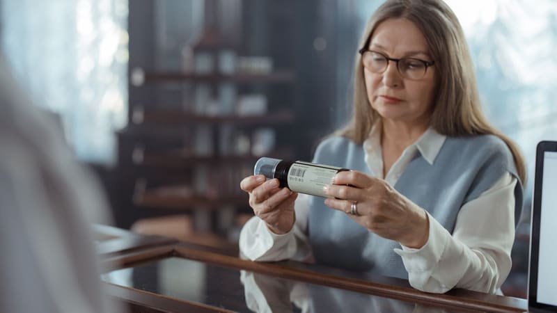 An older woman reading a medicine bottle at a pharmacy counter